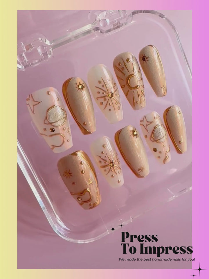 A Video shows A hand holds a clear plastic case displaying 10 press-on nails with a metallic gold and beige celestial design, set against a pink and yellow gradient background with 'Press To Impress' text.