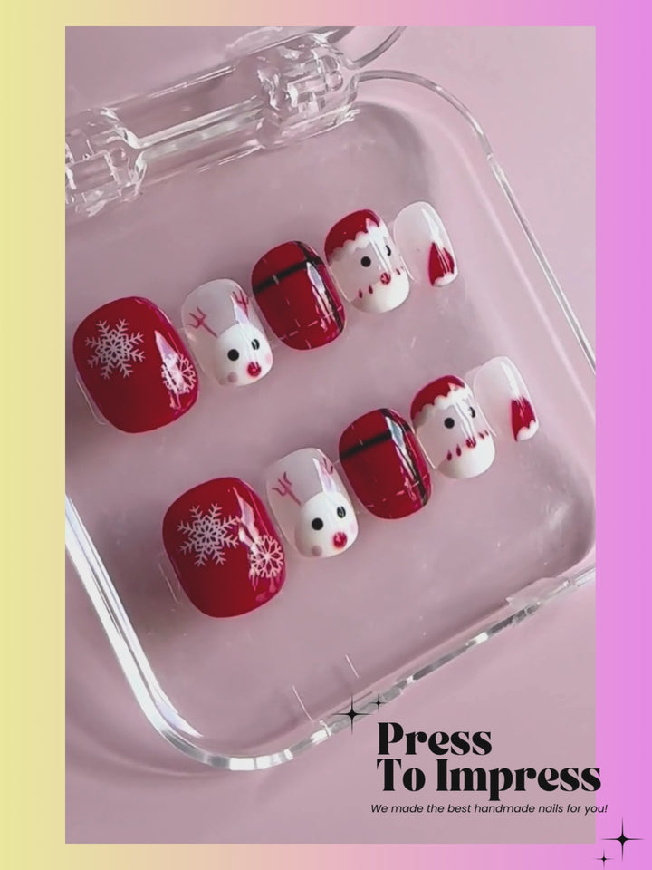 A Video shows A hand holds a clear plastic case displaying 10 Christmas-themed press-on nails. The nails feature red and white holiday designs including snowflakes, Santa faces, plaid patterns, and reindeer.