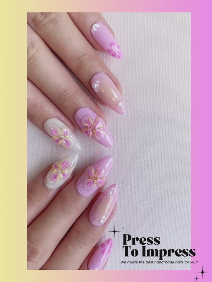 Video shows A hand holds a clear plastic case displaying ten decorative press-on nails. The nails are pastel pink and lavender with floral and geometric patterns, set against a pink-to-yellow gradient background with the text 'Press To Impress'.