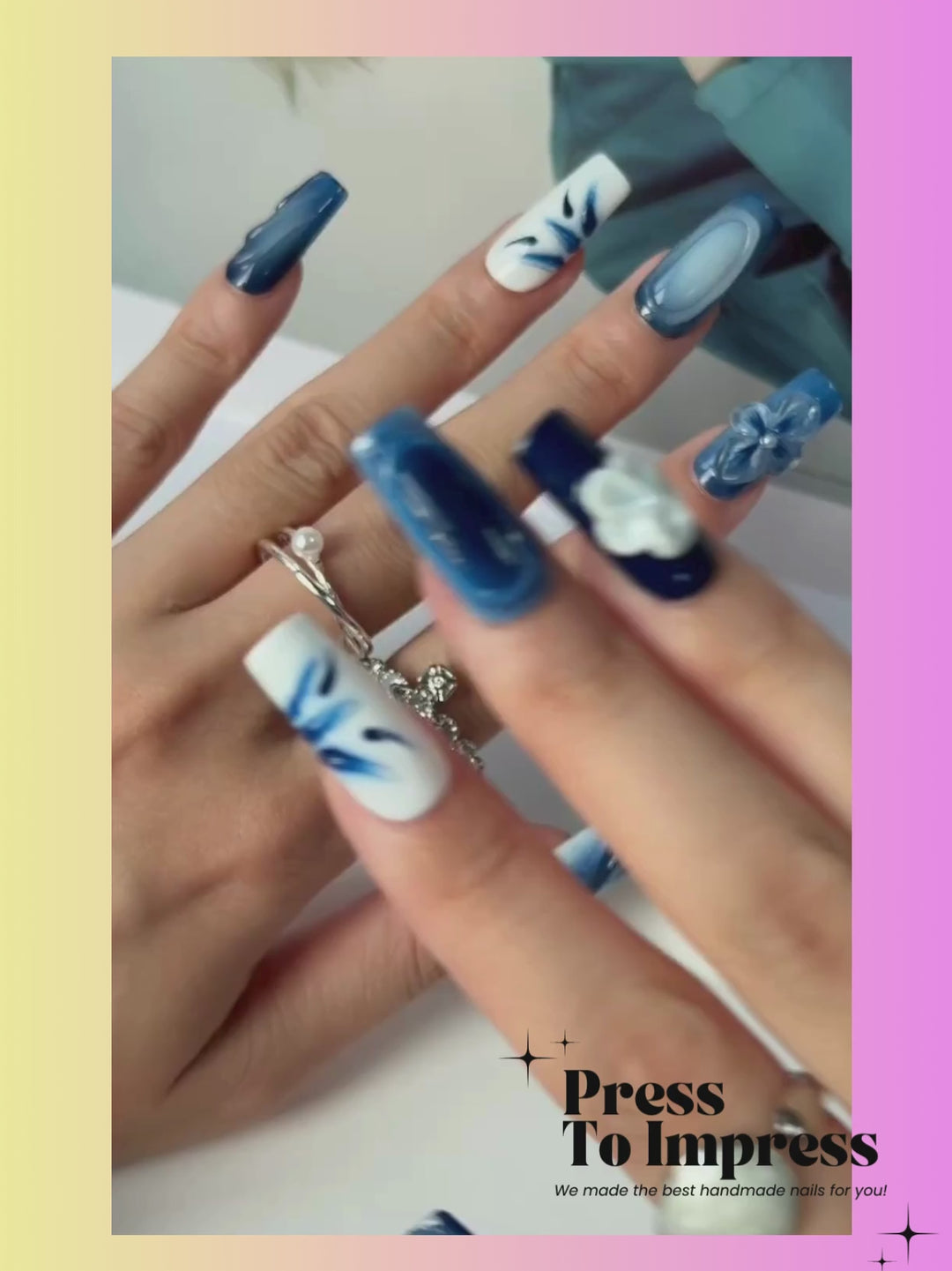 Video shows A hand holds a clear plastic case displaying ten blue and white press-on nails with various designs including swirls, flowers, and solid colors, set against a pink and yellow gradient background with 'Press To Impress' branding.