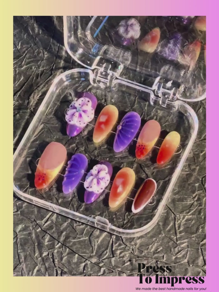 A Video shows A hand holds a clear plastic case displaying ten press-on nails with various designs including purple flowers, orange-to-yellow gradients, and solid black, against a pink and yellow gradient background with 'Press To Impress' branding.
