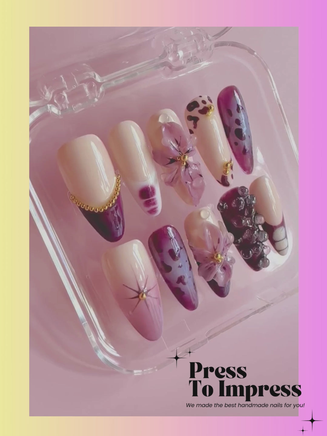 A Video shows A hand holds a clear plastic tray displaying press-on nails with a purple and beige floral/abstract design. The nails feature cream, purple, and dark plum tones with gold and pearl embellishments.