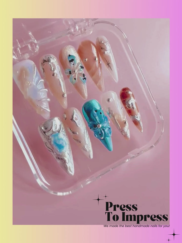 A video shows A hand holds a clear plastic case displaying ten decorative press-on nails with various designs including blue, white, beige, and brown patterns, against a pink and yellow gradient background with 'Press To Impress' text.