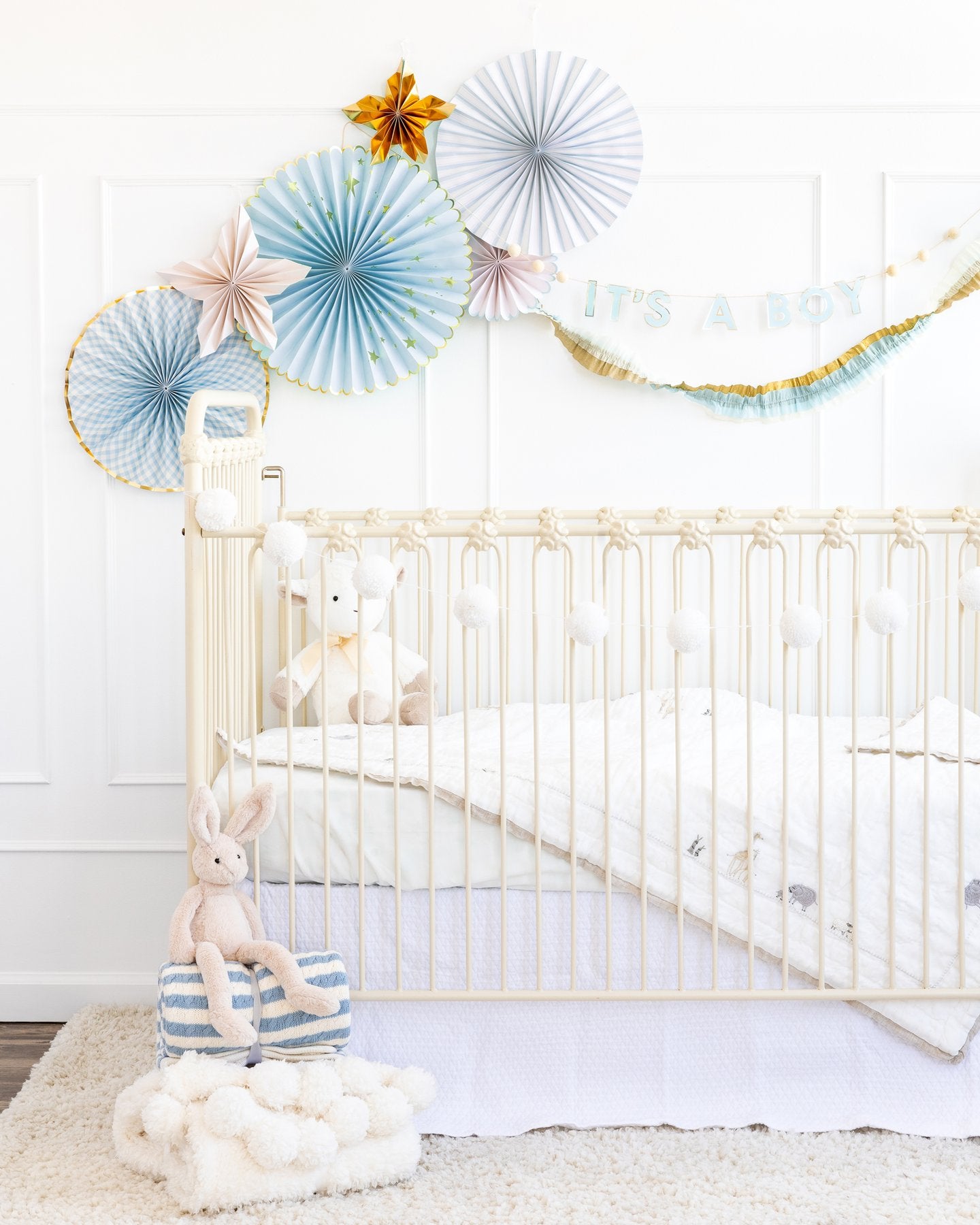 My Mind's Eye Cream/Blue/Gold Crepe Paper Banner hanging over a white baby cot with baby blue fans