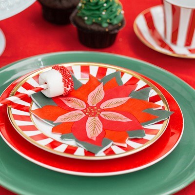 Poinsettia napkin on striped plate with Christmas treat and green dinnerware.