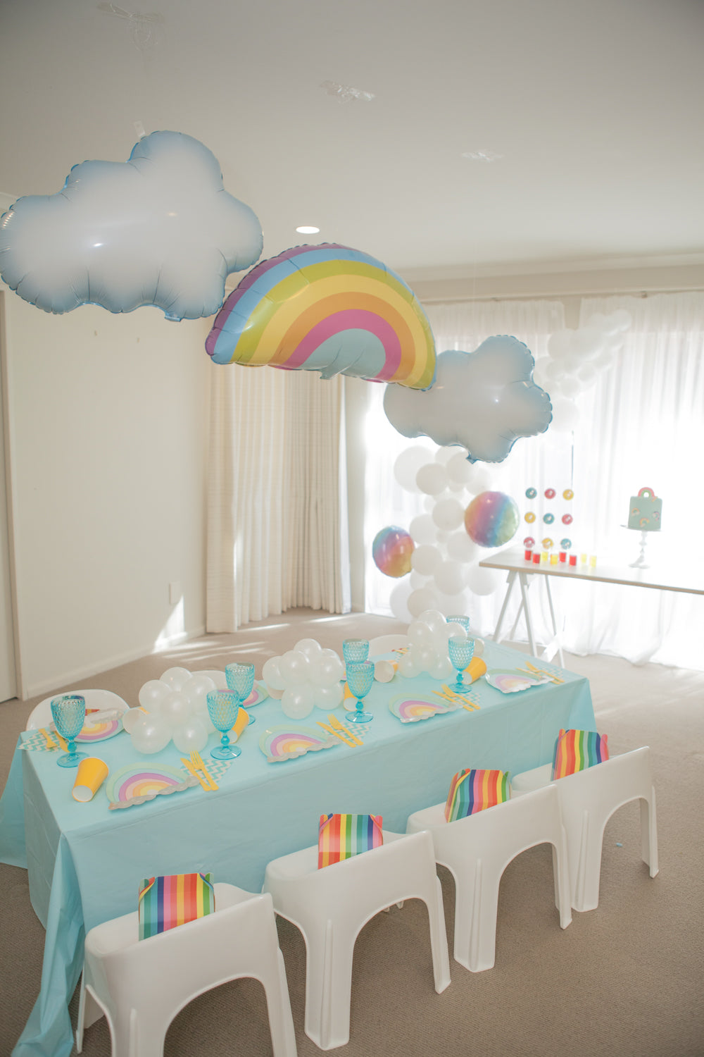 Rainbow Theme Party Set up with rainbow and cloud foil balloon, rainbow plates tableware and White balloon garland