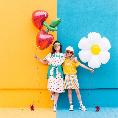Party Decor Two girls holding cherry foil balloon and daisy flower balloon in front of yellow and blue wall