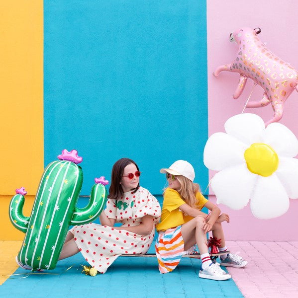 Party Decor Two girls holidy cactus foil balloon, daisy flower foil balloon and a pink leopard foil balloon in front of a colorful wall